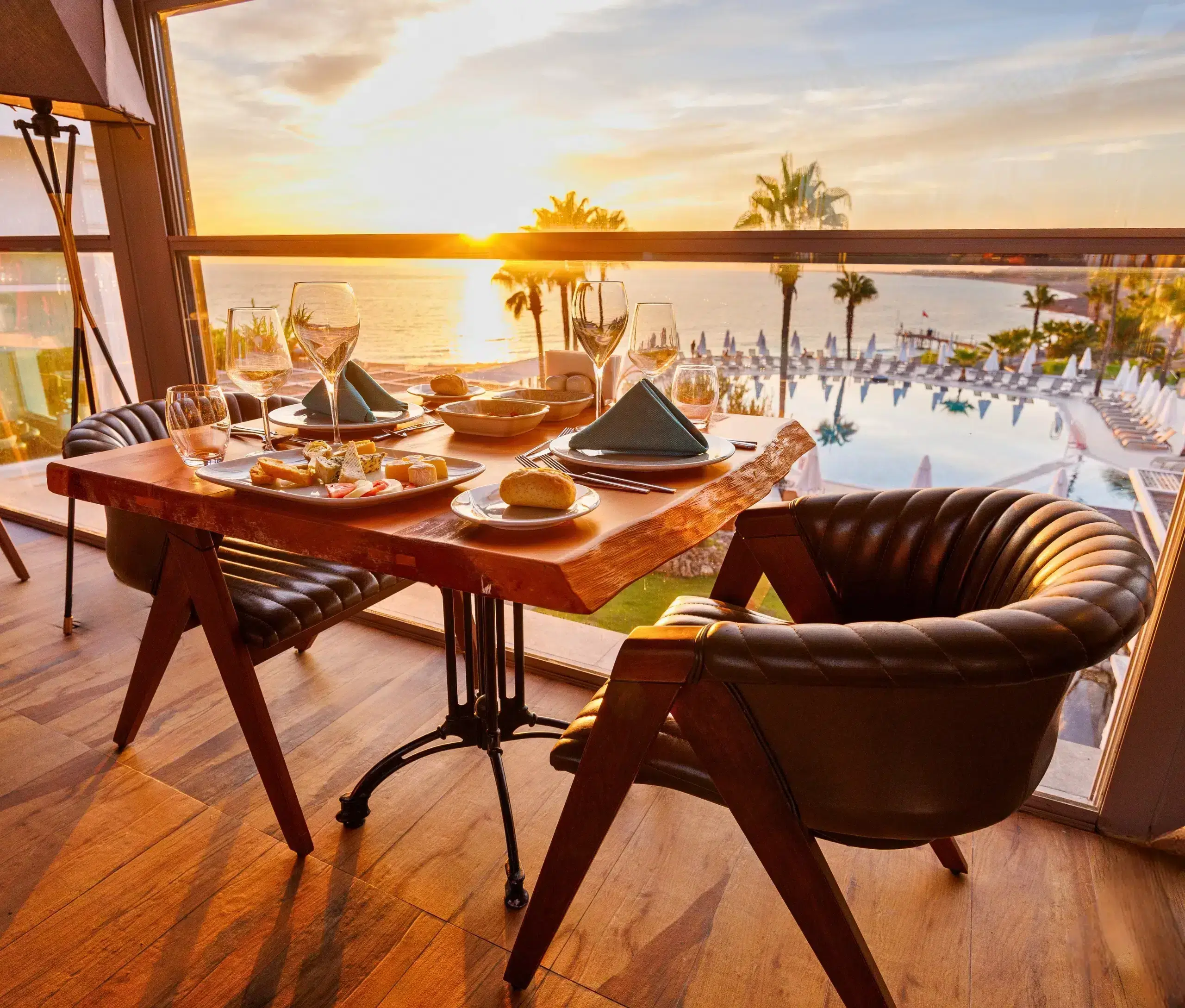 Dinner table set for four with a view of a sunset over a poolside resort.